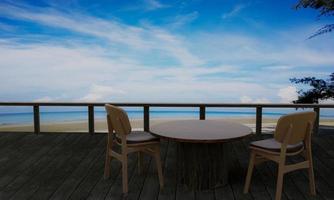 table et chaise pour se détendre prendre le petit déjeuner. terrasse en planches, boutique en bord de mer et plage sur ciel bleu vif et nuage blanc. rendu 3d photo