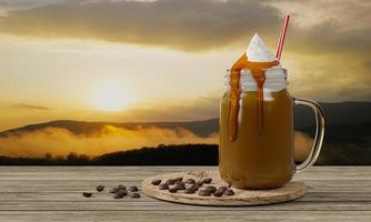 café glacé dans un verre transparent garni de mousse de lait et de caramel saupoudré de poudre de cacao, placez-le sur un billot circulaire. montagne de fond au lever du soleil du matin. rendu 3d photo