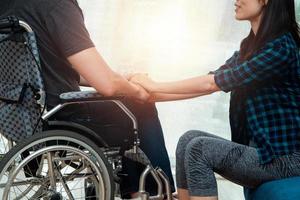 un homme asiatique en fauteuil roulant à la maison après un accident de voiture et sa femme pour l'encourager. le concept de soins mutuels et les nouvelles technologies ont fait des personnes handicapées l'égalité dans la société. photo