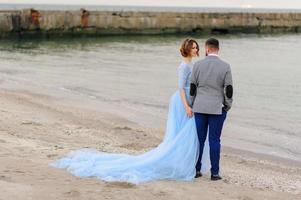 séance photo de mariage d'un couple au bord de la mer. robe de mariée bleue sur la mariée.