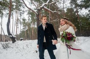 la joyeuse mariée et le marié en pulls tricotés beiges se promènent dans la forêt enneigée. mariage d'hiver photo