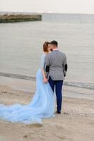 séance photo de mariage d'un couple au bord de la mer. robe de mariée bleue sur la mariée.