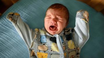 un petit garçon nouveau-né regarde la fenêtre de son berceau. un garçon né à 8 mois de gestation. il y a un costume tricoté sur le garçon. photo