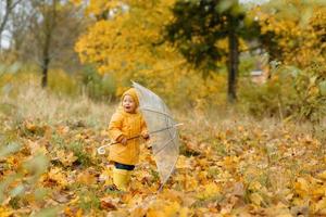 une petite fille marche avec un parapluie dans des bottes en caoutchouc jaunes et un imperméable imperméable. promenade d'automne. photo