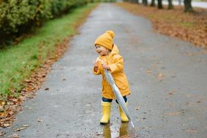 une petite fille marche avec un parapluie dans des bottes en caoutchouc jaunes et un imperméable imperméable. promenade d'automne. photo