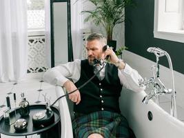 bel homme mature et courageux écossais en kilt et costume parlant au téléphone depuis la maison. style, mode, style de vie, verrouillage, culture, concept ethnique. photo