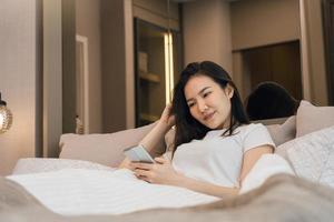 femme asiatique au lit vérifiant les applications sociales avec smartphone le matin. photo