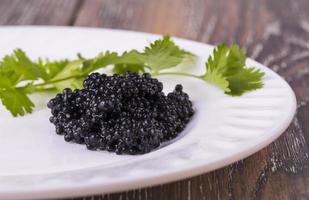 caviar noir sur une assiette blanche avec des herbes sur bois photo
