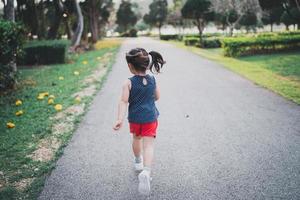 heureuse petite fille asiatique souriante. petite fille qui court au coucher du soleil heureuse petite fille souriante. petite fille qui court au coucher du soleil. jolie petite fille qui court au jardin de l'aire de jeux. photo