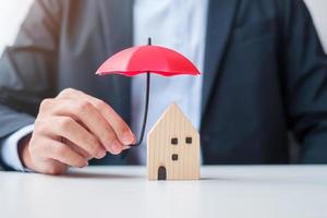 main d'homme d'affaires tenant le modèle de maison en bois de couverture de parapluie rouge. concepts d'immobilier, d'assurance et de propriété photo