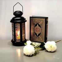 la lanterne du ramadan est de couleur noire, lumineuse, décorée de motifs en bois, à côté du saint coran, avec quelques roses blanches photo