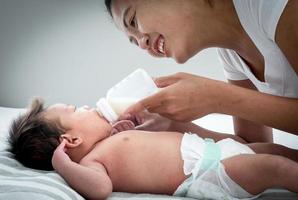 portrait d'une mère asiatique nourrit le nouveau-né asiatique australien de trois semaines avec du lait maternisé à partir d'une bouteille, concept de maternité et d'enfance ou bébé allongé sur le lit blanc. photo