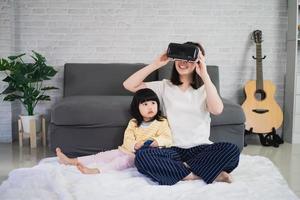 mère et fille asiatiques jouent au jeu vr pour se divertir ensemble à la maison, famille joyeuse ensemble dans la maison en vacances. concept de technologie vr metaverse famille heureuse. photo