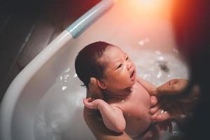 petite fille asiatique heureuse de prendre un bain par sa mère à la maison, douche de bébé enfant asiatique. concept de famille de bébé. photo
