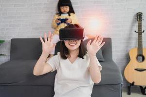 mère et fille asiatiques jouent au jeu vr pour se divertir ensemble à la maison, famille joyeuse ensemble dans la maison en vacances. concept de technologie vr metaverse famille heureuse. photo