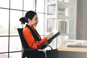 Une jeune femme d'affaires asiatique adulte écrit sur un journal intime au bureau le jour photo