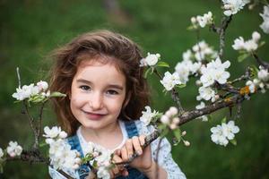 une jolie petite fille de 5 ans dans un verger de pommiers blancs en fleurs au printemps. printemps, verger, floraison, allergie, parfum printanier, tendresse, soin de la nature. portrait photo