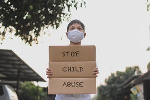 un garçon asiatique portant un masque médical tenant un panneau à lettres dit arrêter la campagne contre la maltraitance des enfants photo