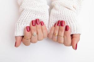 vernis gel pour manucure de couleur rouge avec des étincelles sur les mains féminines avec des anneaux et un pull photo