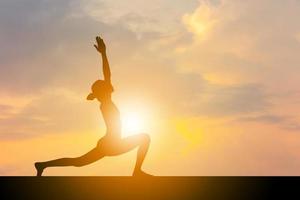 silhouette de jeune femme avec un tracé de détourage pratiquant le yoga exercice relaxant au coucher du soleil, liberté et concepts de détente. photo