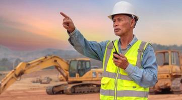 un ingénieur d'âge moyen utilise un talkie-walkie sur le chantier, un aîné asiatique supervise le travail du soir. photo