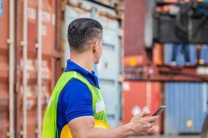 un ingénieur utilise un téléphone portable, un ouvrier industriel utilise un smartphone mobile dans la cargaison de conteneurs de l'industrie photo