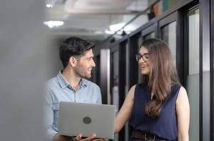 un jeune homme d'affaires tenant un ordinateur portable et marchant discute du travail avec une équipe féminine, une équipe commerciale de collègues se réunissant dans un bureau créatif photo