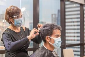 jeune homme se faisant couper les cheveux par un coiffeur, coiffeur utilisant des ciseaux et un peigne, coiffeur et client portant un masque de protection en raison de la pandémie de coronavirus, nouveaux concepts normaux photo