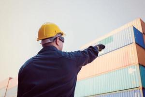 un ouvrier portant un casque et un gilet de sécurité pointe vers le ciel, le contremaître contrôle le chargement des conteneurs de la cargaison photo