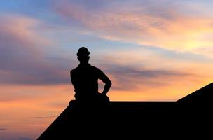 silhouette de contremaître dans un casque assis sur une boîte contenant avec ciel coucher de soleil photo