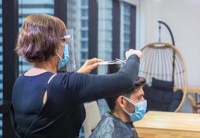 jeune homme se faisant couper les cheveux par un coiffeur, coiffeur utilisant des ciseaux et un peigne, nouveau concept normal photo