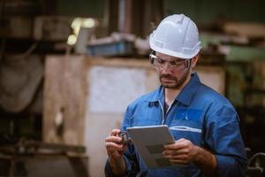 ingénierie de l'industrie portant un contrôle uniforme de sécurité faisant fonctionner une machine de meulage de tour contrôlée par ordinateur travaillant dans l'usine de l'industrie. photo