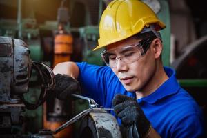 ingénierie de l'industrie portant un contrôle uniforme de sécurité faisant fonctionner une machine de meulage de tour contrôlée par ordinateur travaillant dans l'usine de l'industrie. photo