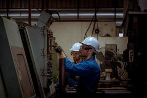 ingénierie de l'industrie portant un contrôle uniforme de sécurité faisant fonctionner une machine de meulage de tour contrôlée par ordinateur travaillant dans l'usine de l'industrie. photo