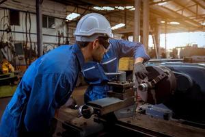 ingénierie de l'industrie portant un contrôle uniforme de sécurité faisant fonctionner une machine de meulage de tour contrôlée par ordinateur travaillant dans l'usine de l'industrie. photo