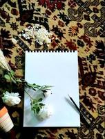 croquis de couleur blanche avec un crayon pour dessiner placé sur un tapis décoratif fait main et à côté se trouvent des fleurs blanches et des cristaux de sel photo