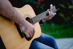 photo d'un guitariste, d'un jeune homme jouant de la guitare assis dans un jardin naturel, concept musical