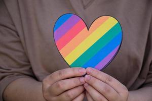 deux coeurs en papier de couleur arc-en-ciel tiennent dans les mains de la personne lgbt, concept pour les célébrations des communautés lgbtq dans le mois de la fierté à travers le monde photo