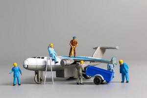 équipe de travailleurs miniatures vérifiant et réparant l'avion sur fond gris photo