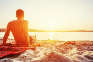 homme assis sur le sable au coucher du soleil photo