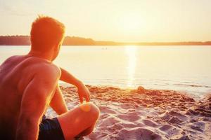 homme assis sur le sable au coucher du soleil photo