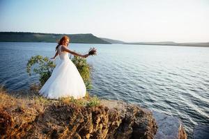 mariée avec un bouquet de fleurs près de l'eau photo