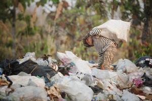 un pauvre garçon ramasse des ordures pour les vendre. vie et mode de vie des pauvres concept de travail des enfants, pauvreté, environnement. séparation des déchets. photo