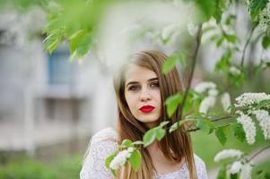 portrait de belle fille aux lèvres rouges au jardin de fleurs de printemps, porter une robe rouge et un chemisier blanc. photo