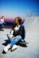 jeune adolescente urbaine avec planche à roulettes, porter des lunettes, une casquette et un jean déchiré au skate park le soir. photo