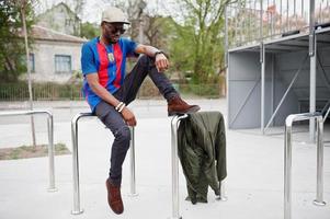 garçon afro-américain élégant portant une casquette, un t-shirt de football et des lunettes de soleil posés sur des balustrades en acier. portrait d'homme sportif noir. photo