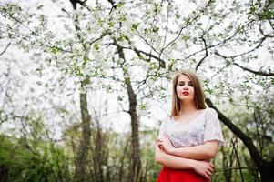 portrait de belle fille aux lèvres rouges au jardin de fleurs de printemps, porter une robe rouge et un chemisier blanc. photo