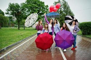 groupe de six filles s'amusant à la fête de poule, avec parapluie sous la pluie et ballons. photo