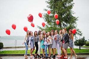 onze demoiselles d'honneur à l'allure étonnante avec une superbe mariée posant avec des ballons rouges en forme de cœur sur le trottoir contre le lac en arrière-plan. photo