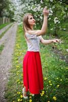 portrait de belle fille aux lèvres rouges au jardin de fleurs de printemps, porter une robe rouge et un chemisier blanc. photo